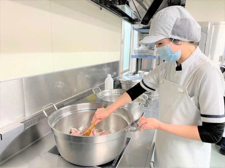 施設の厨房で職員が大型調理鍋で食事を準備している様子